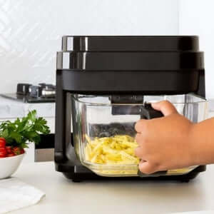 Person using a black glass air fryer with a transparent cooking bowl, preparing fresh fries for a healthier, oil-free cooking experience.