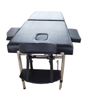 Black massage table with padded armrests, integrated face hole, and sturdy wooden legs with a lower storage shelf, designed for professional spa and therapy sessions.