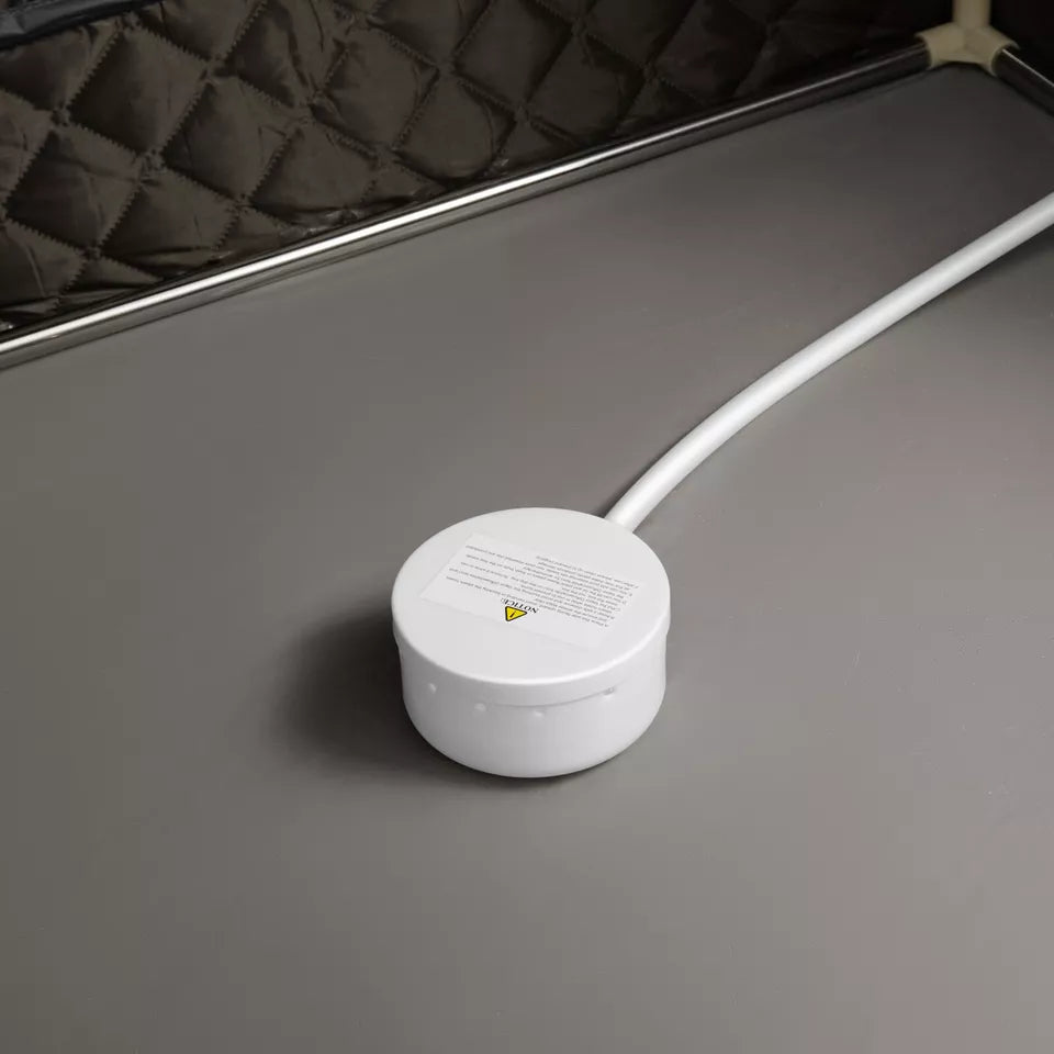 "Close-up of a white steam outlet or control knob inside a sauna tent, placed on a heat-resistant grey surface. The quilted walls in the background emphasize the insulated interior design of the tent