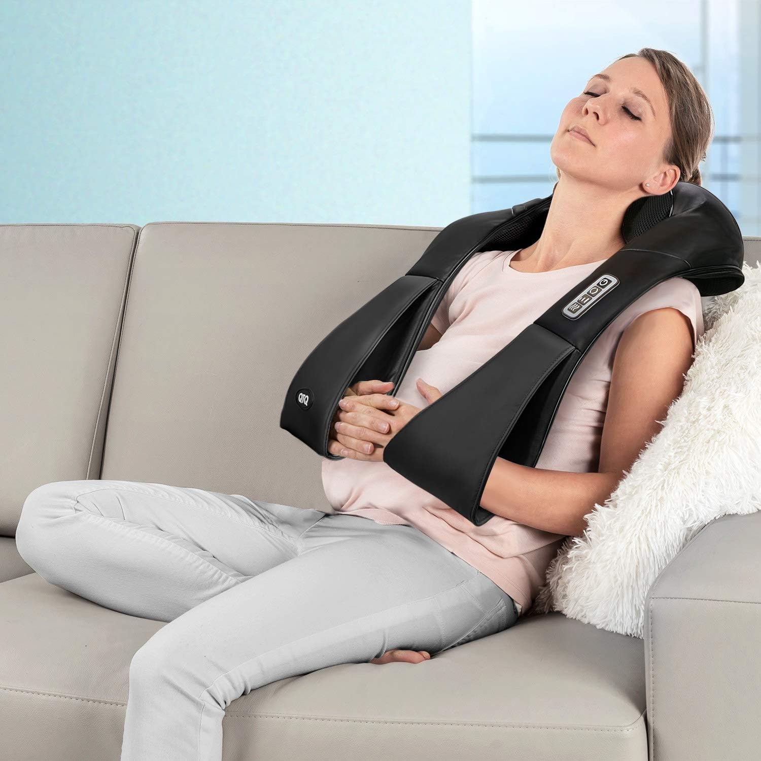 Woman using electric neck and shoulder massager with heat while relaxing on the couch for deep tissue relief and relaxation