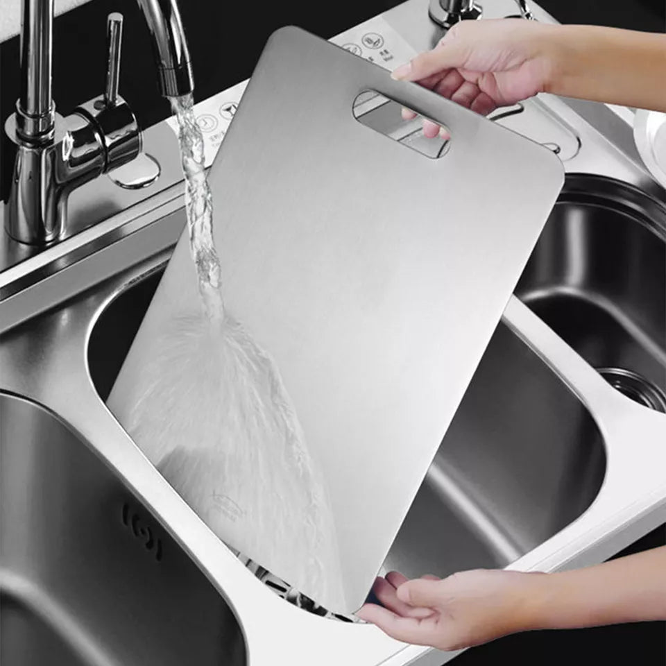 "Hands placing a Titanium Cutting Board into a kitchen sink for rinsing, highlighting its lightweight, easy-to-clean design and stainless finish suitable for everyday use.