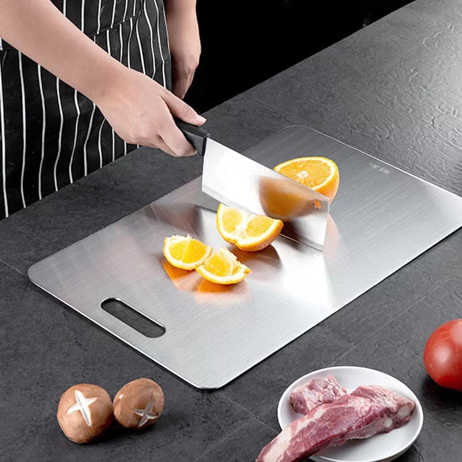 "Person slicing yellow potatoes on a Titanium Cutting Board placed on a modern kitchen counter. Surrounding ingredients include onions, tomatoes, and raw meat, highlighting the board’s versatility for food prep