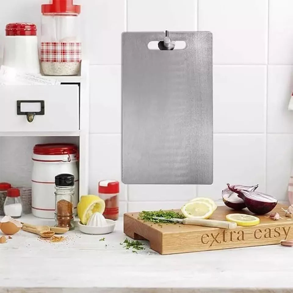 "Titanium Cutting Board hanging on a white kitchen wall above a countertop with vegetables, spices, and cooking utensils. Showcases the board’s modern design, space-saving handle, and premium kitchen appeal.