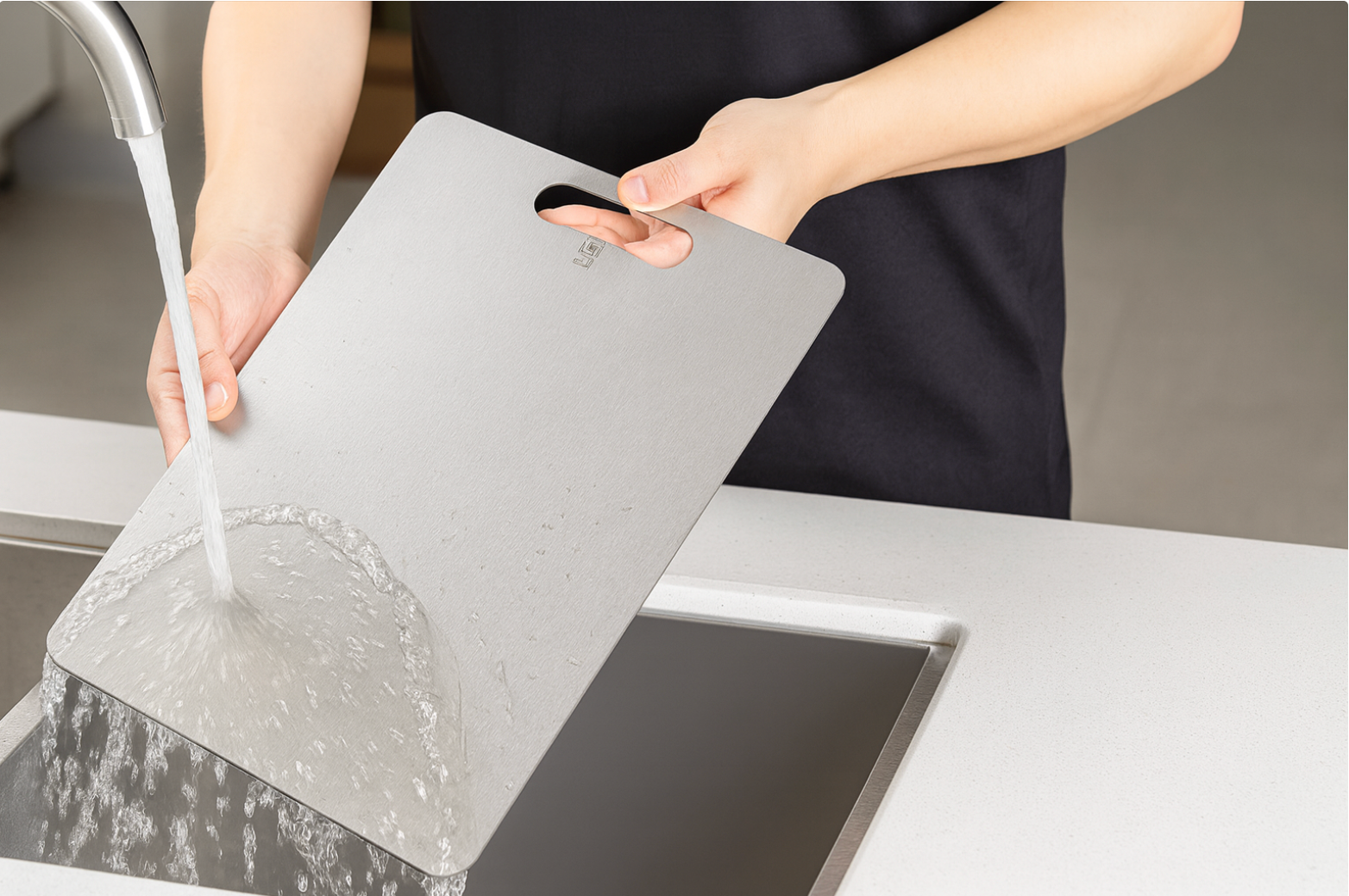Person washing a titanium cutting board under running water in a modern kitchen sink for easy hygiene and durability.