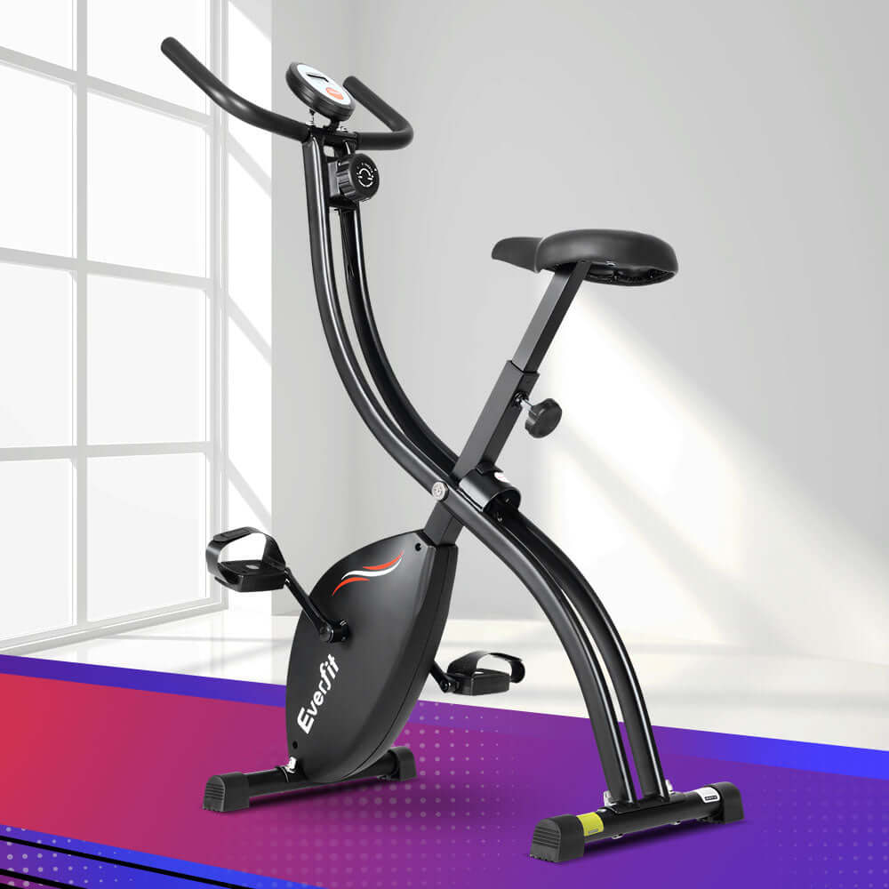Black foldable exercise bike set up in a bright home gym, featuring a sturdy frame, cushioned seat, and digital display for effective cardio workouts.