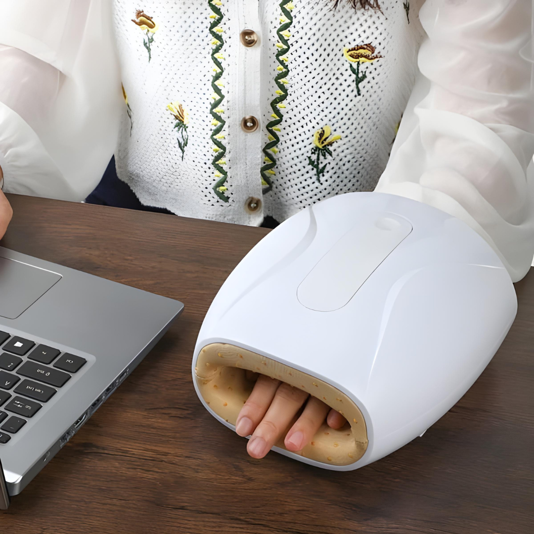 User operating a white hand massager with heat and compression next to a laptop, ideal for relieving wrist pain during work breaks