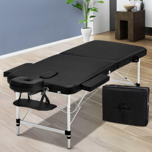 Black portable massage table with adjustable headrest and sturdy foldable metal legs, accompanied by a carrying case, ideal for professional or home massage sessions.