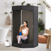 Woman sitting inside a black portable sauna tent in a modern living room setting, enjoying a steam or infrared session. The sauna tent is zippered and fully enclosed, designed for personal at-home wellness and relaxation.